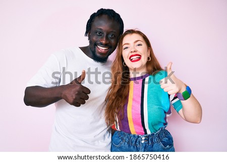 Interracial couple wearing casual clothes success sign doing positive gesture with hand, thumbs up smiling and happy. cheerful expression and winner gesture. 