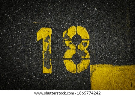 Grey asphalt road, yellow painted number eighteen on grey street, yellow lines like a corner on the road, space for text 