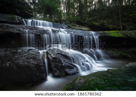 Waterfall landscape. Focus on waterfall, blurred leaves. Beautiful waterfall in tropical rainforest with  rocks and blurred leaves.  Adventure destination in Asia. Slow shutter speed technique.