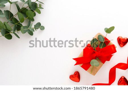 Gift box wrapped in brown paper decorated with eucalyptus branch, red hearts and red bow on white, copy space, top view.