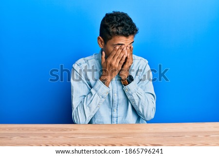 Young handsome african american man wearing casual clothes sitting on the table rubbing eyes for fatigue and headache, sleepy and tired expression. vision problem 