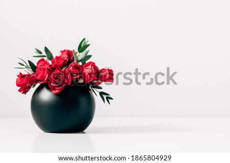 Red roses in black vase on background of white wall. Front view.