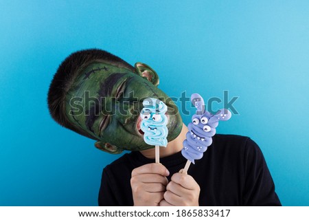 Cute boy with a painted face on a blue background. Meringue on a stick in the hands of a child. Children's holiday