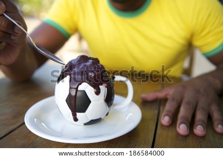 Brazilian soccer player sitting at a restaurant table eating acai from a football cup