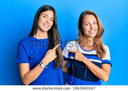 Hispanic family of mother and daughter wearing casual clothes over blue background cheerful with a smile on face pointing with hand and finger up to the side with happy and natural expression 