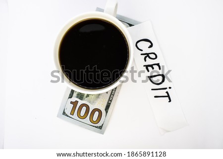 A Cup of coffee is on a hundred-dollar bill next to a piece of paper with the word credit written on it. Concept photo