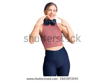 Beautiful caucasian young woman wearing gym clothes and using headphones smiling cheerful showing and pointing with fingers teeth and mouth. dental health concept. 
