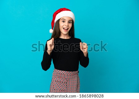 Little girl with Christmas hat isolated on blue background celebrating a victory in winner position