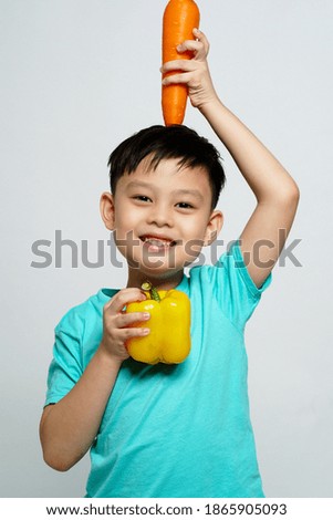 A boy holding carrot put on his head and paprika under his chin