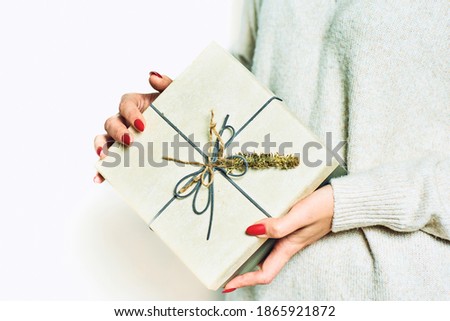 Close up shot of female hands holding a gift wrapped with gold ribbon. Gift in the hands of a woman in gray cloths on the isolate background. Shallow depth of field with focus on the box.