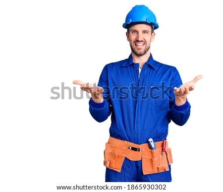 Young handsome man wearing worker uniform and hardhat smiling cheerful offering hands giving assistance and acceptance. 