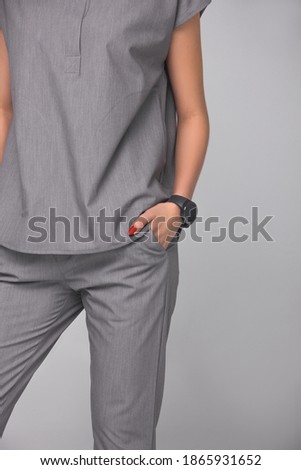 close-up of stylish nurse's gray medical costume. young doctor teacher is standing with hands in her pockets on gray wall background. medical fashion concept. free space