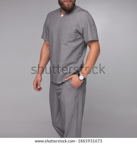 close-up gray medical shirt of young stylish nurse male with beard which is standing on white wall background with strong hands. medical fashion concept. free space 
