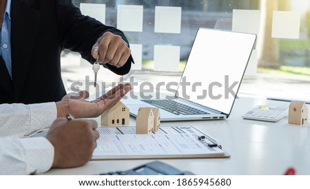 Real estate agent holds house keys for clients after signing contract in office, real estate concept with house model and laptop on desk.