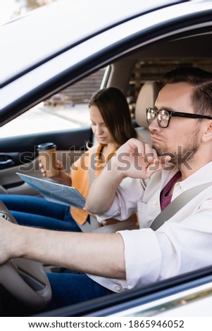 Pensive man driving car near wife with coffee to go and map on blurred background 