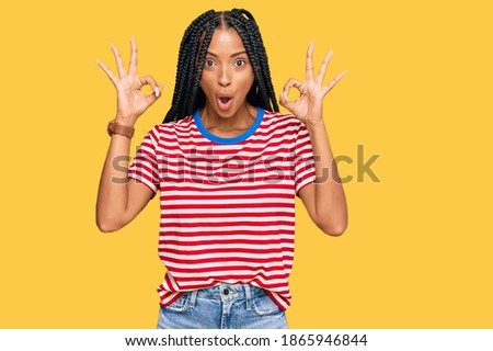 Beautiful hispanic woman wearing casual clothes looking surprised and shocked doing ok approval symbol with fingers. crazy expression 