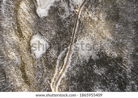 Aerial view of the road and taiga forest in winter on a sunny bright day. Abstract landscape of northern nature with drone. Local map
