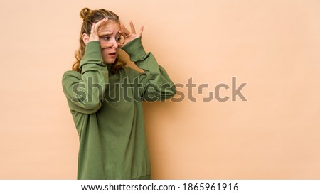 Young caucasian woman isolated on beige background keeping eyes opened to find a success opportunity.