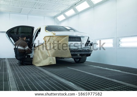 a worker prepares a white car for painting in a car painting booth	 Royalty-Free Stock Photo #1865977582