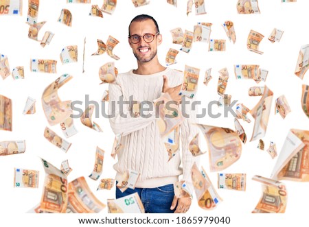 Young handsome man wearing casual clothes and glasses cheerful with a smile of face pointing with hand and finger up to the side with happy and natural expression on face