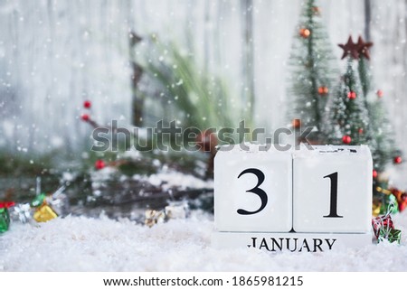 White wood calendar blocks with the date January 31st and Christmas decorations with snow. Selective focus with blurred background. 