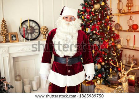 Portrait of Santa Claus with glasses near the fireplace and christmas tree with gifts. New year and Merry Christmas , happy holidays concept