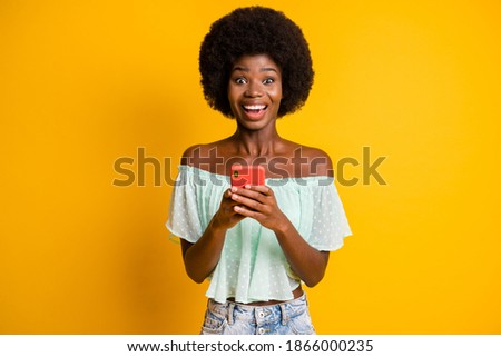 Photo portrait of excited girl with open mouth holding phone in two hands isolated on vivid yellow colored background