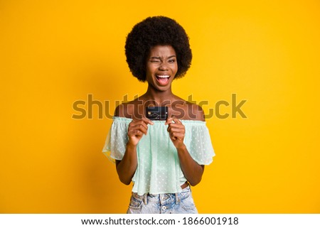 Photo portrait of winking woman holding credit card in two hands isolated on vivid yellow colored background