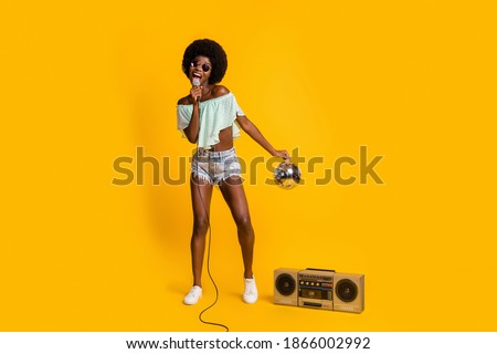 Full length body size photo of black skinned girl performing song with disco ball at concert with boombox isolated on vibrant yellow color background