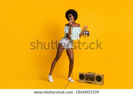 Full length body size photo of black skinned girl singing keeping disco ball listening boombox isolated on vivid yellow color background