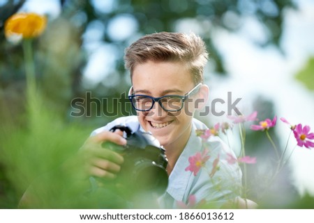 Funny boy teenager 15 years old with a camera takes pictures in the park in summer
