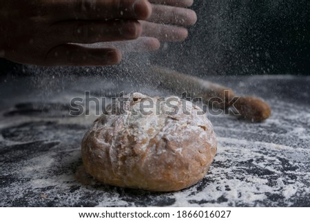 Baker clap hands with flour splash on fresh bread.Bakery concept lifestyle with rolling on floury dark background. Royalty-Free Stock Photo #1866016027