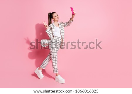 Photo portrait full body view of woman taking selfies on the go showing v-sign isolated on pastel pink colored background