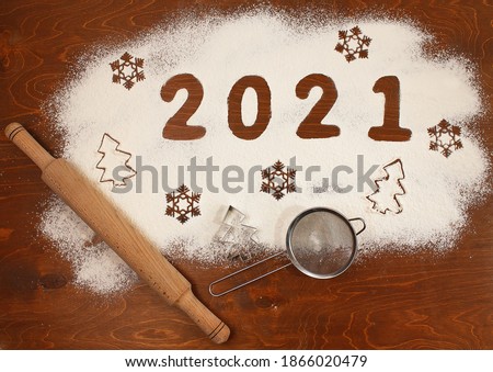 happy new year 2021 concept. numbers 2021, figures of snowflakes and firs are made of flour on a wooden table, next to a rolling pin and a sieve
