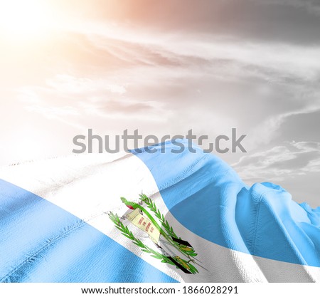 Guatemala national flag cloth fabric waving on beautiful grey sky.