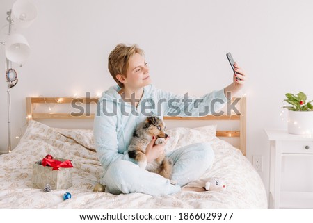 Young happy Caucasian woman taking selfie picture with cute puppy dog pet on smartphone. Distant remote holiday celebration online on Internet. Video call with family and friends. 