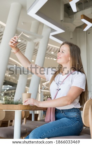 Cute cheerful woman make selfie on her phone while sitting in a cafe waiting for her coffee. Summer sunny day