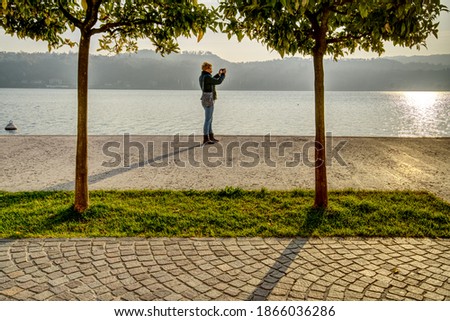 A middle aged caucasian woman reaching for a fruit of the orange tree on the shore of the Garda Lake in Italy in autumn of 2020