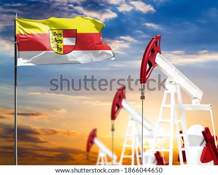 Oil rigs against the backdrop of the colorful sky and a flagpole with the flag of Carinthia. The concept of oil production, minerals, development of new deposits.