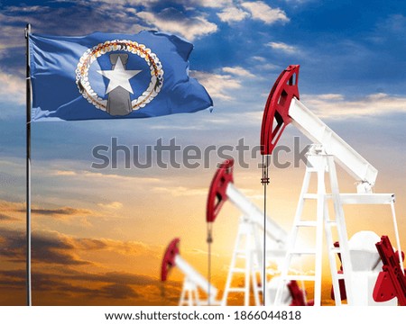 Oil rigs against the backdrop of the colorful sky and a flagpole with the flag of Northern Mariana Islands. The concept of oil production, minerals, development of new deposits.