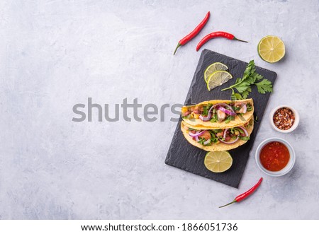 two Mexican street tacos with chicken, onions, chili peppers, corn and beans are shot on a serving blackboard with a lime wedge and spices. Top view and copy space
