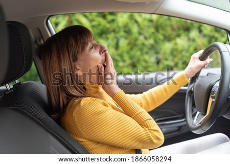 Tired woman yawning behind steering wheel of car
