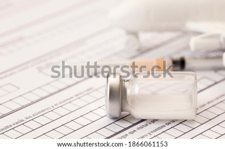 aluminum and glass vaccine vial, syringe, white airplane mockup on top of airport control form