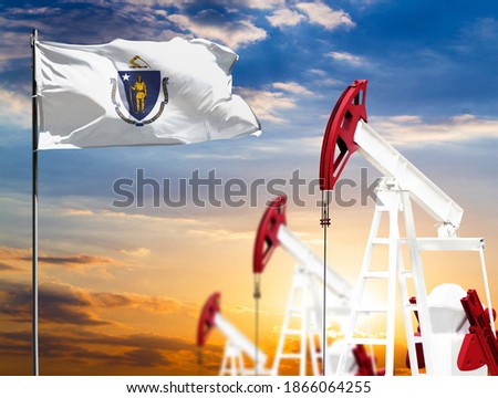 Oil rigs against the backdrop of the colorful sky and a flagpole with the flag State of Massachusetts. The concept of oil production, minerals, development of new deposits.
