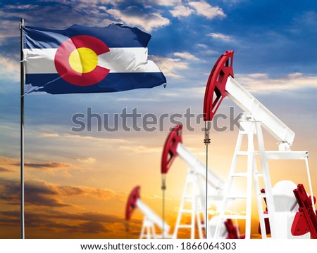 Oil rigs against the backdrop of the colorful sky and a flagpole with the flag State of Colorado. The concept of oil production, minerals, development of new deposits.
