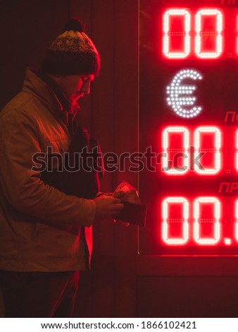 Young man standing near exchange point in the dark red light of exchange rate with money in hands
