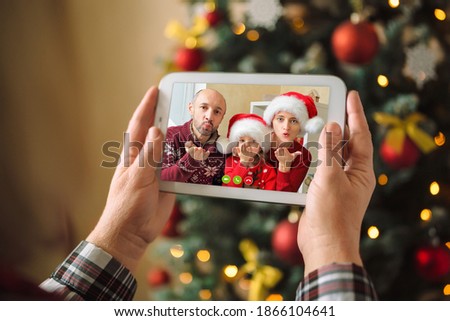 Children congratulate their parents via video conference. A woman holds a digital tablet in her arms and see how they blow a kiss a greeting on Christmas eve.