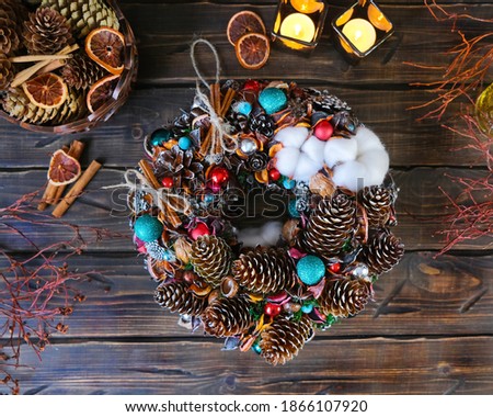 Christmas wreath made of natural materials with colorful balls on a wooden background with burning candles.