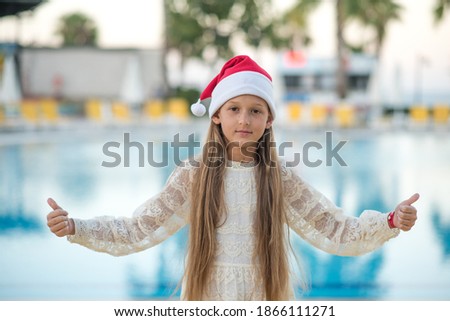 Happy little girl in Santa Claus hat near the pool. We celebrate Christmas in warm countries
