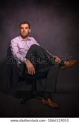 Portrait of a young handsome male businessman sitting in armchair in dark studio room.